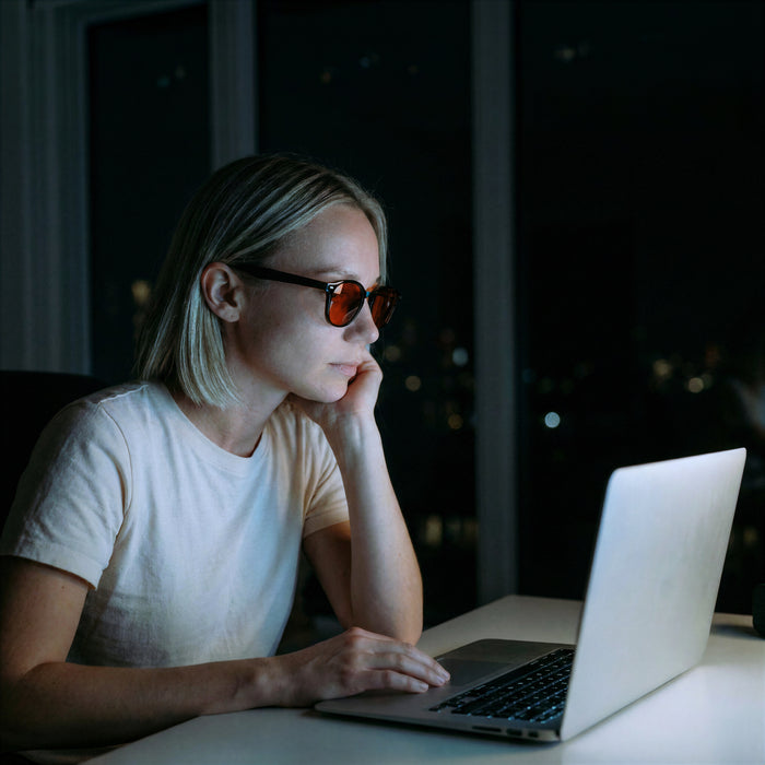 Vrouw kijkt 's avonds op haar laptop met een blauw licht bril met oranje glazen