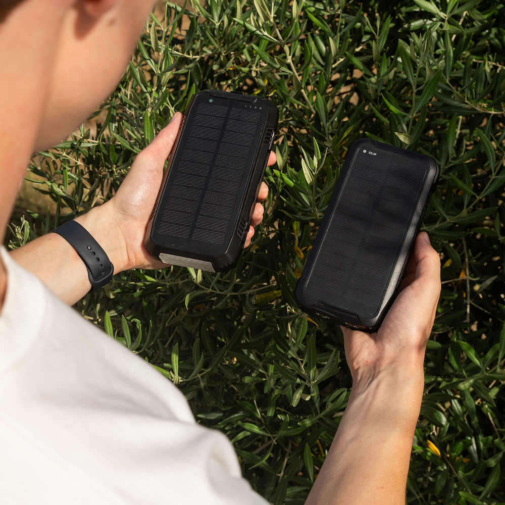Twee Banky solar powerbanks met zonnepaneel vastgehouden in de handen, buiten in de natuur