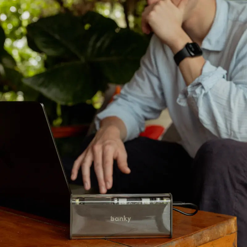 Laptop powerbank 100W van Banky naast een laptop op een houten tafel buiten, ideaal voor op reis