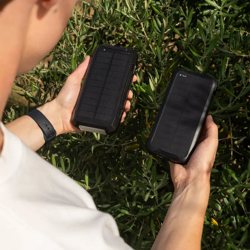 Banky solar powerbank en telefoon in de hand boven groene struiken