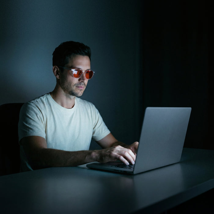 Man werkt 's avonds op zijn laptop met de oranje glazen op