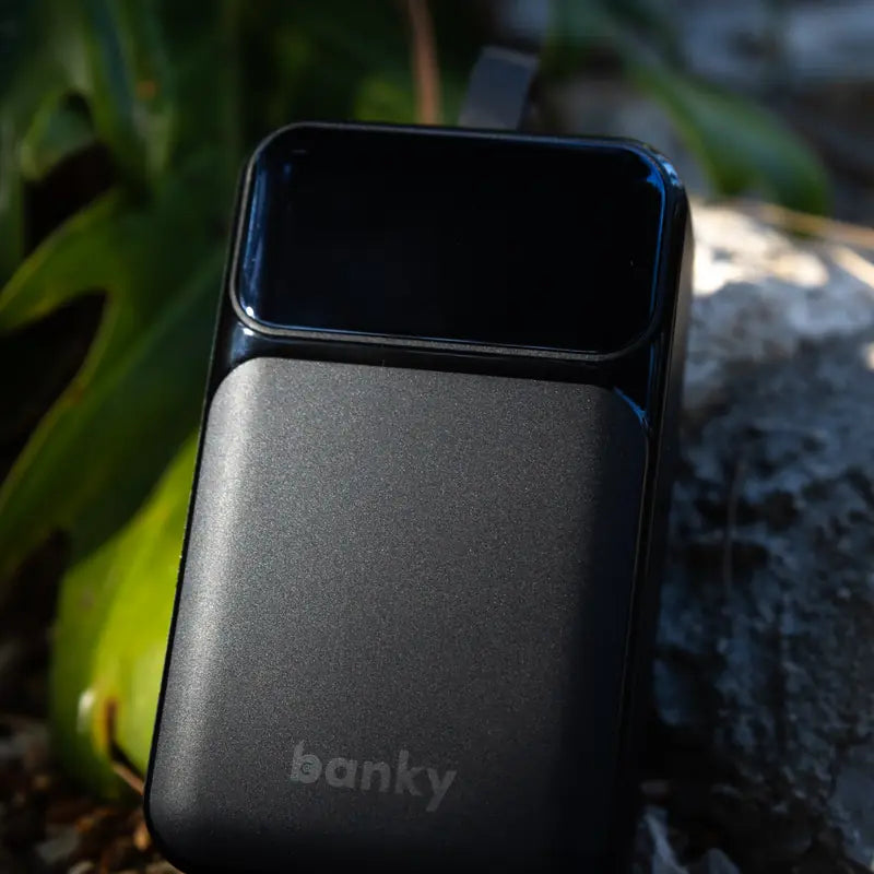 Banky 65W laptop powerbank 27.000 mAh op een rots tussen groene bladeren, geschikt voor het vliegtuig