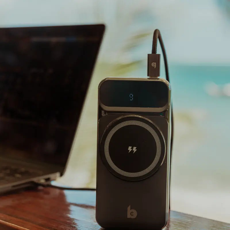 MagSafe powerbank van Banky rechtop naast een laptop aan zee, compact genoeg voor in het vliegtuig