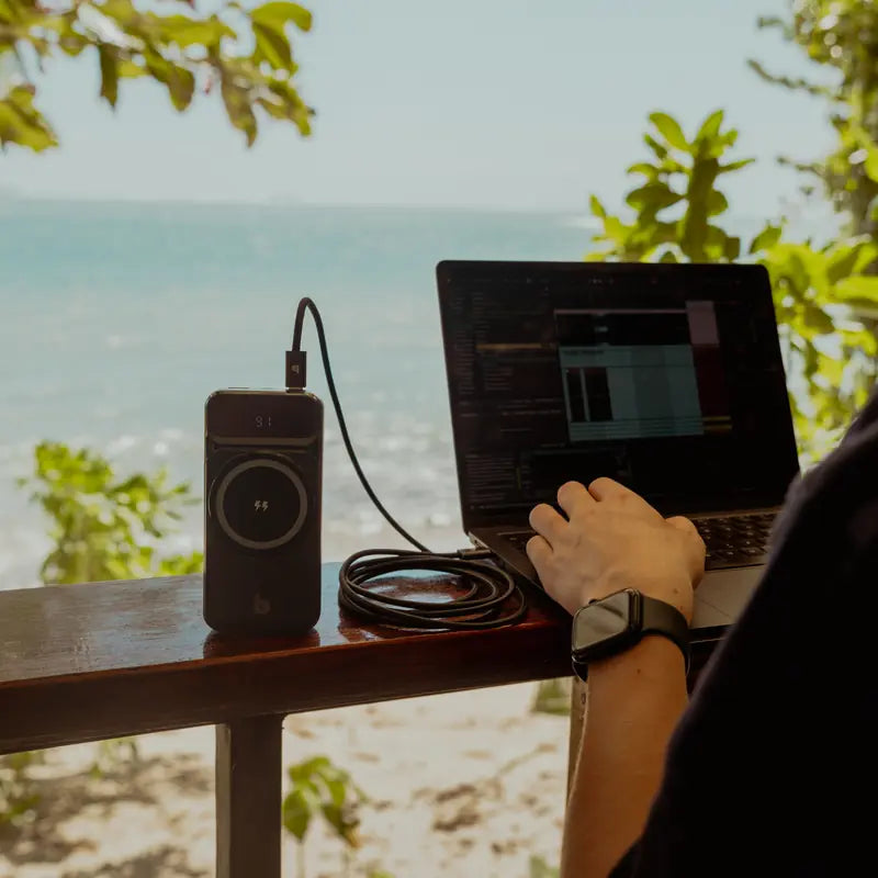 Banky powerbank voor laptop op een balkonrand aan zee, aangesloten op een laptop